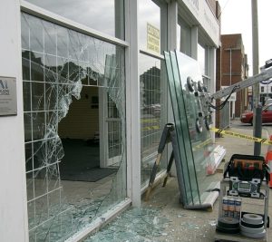 "Kırık vitrin camı değişimi ve yeni cam panellerin montaj hazırlığı, sokak seviyesinde dükkan cam tamiri sahnesi.
